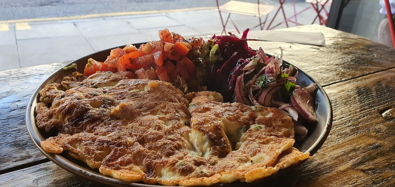 A golden omelette at Nilly's Cafe plated with chopped tomato, dressed leaves and red onion salad by the window.