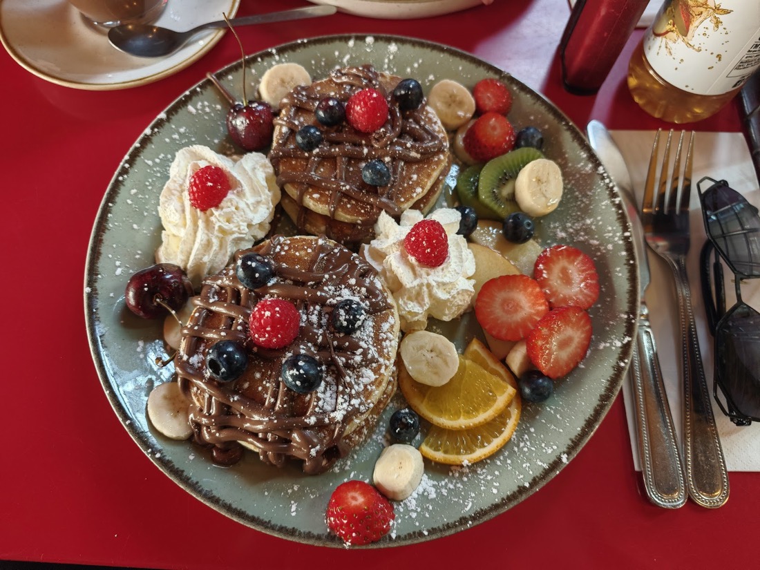 Two stacks of pancakes at Nilly's Cafe drizzled with chocolate sauce, dusted with icing sugar and piled with strawberries, blueberries, banana and cream.